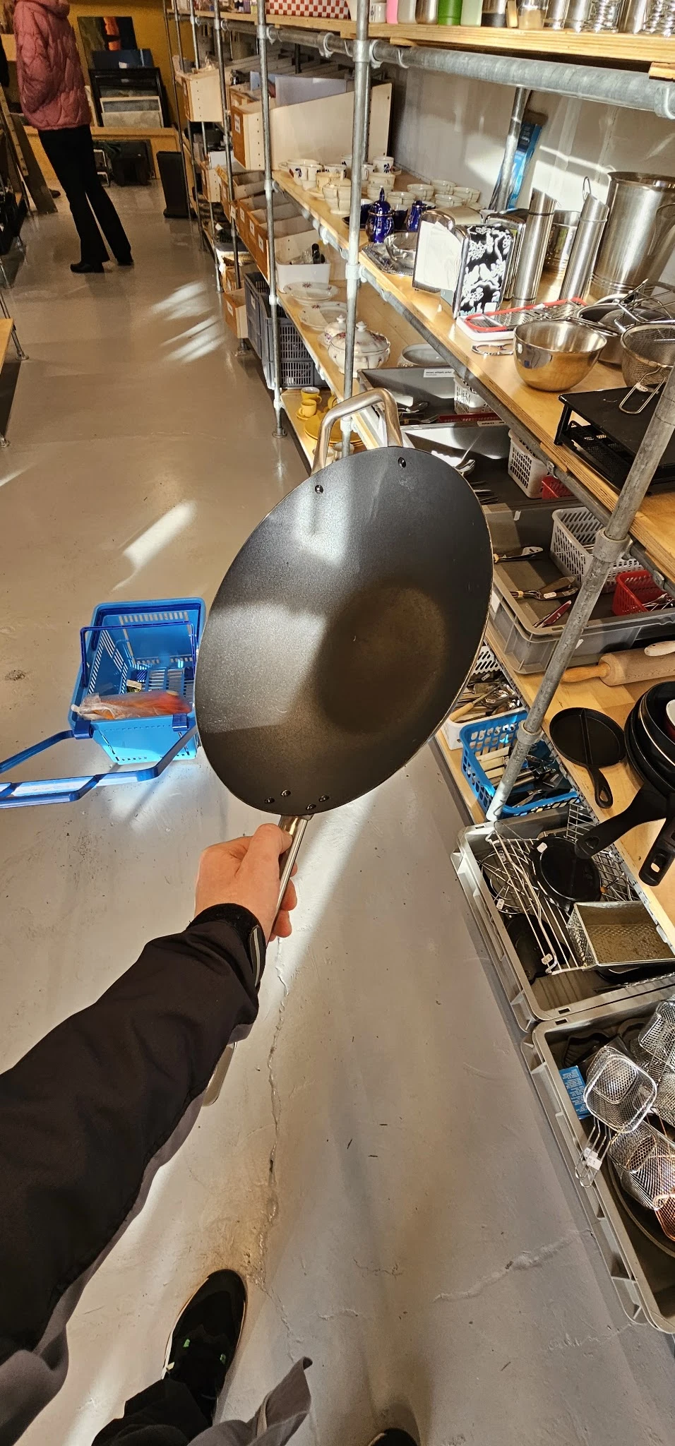 Grote zwarte wokpan met stalen handvat, gehouden in hand tegen neutrale achtergrond