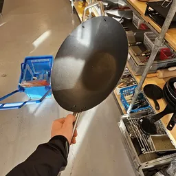Grote zwarte wokpan met stalen handvat, gehouden in hand tegen neutrale achtergrond
