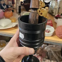 Close-up van een zwarte mortelaar met zware stenen stamper in een hand