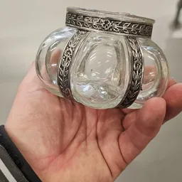 Close-up van een glazen potje met zilveren decoratieve band, gehouden in een hand