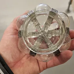 Close-up van een rond glazen decoratief item met metalen details en paars/roze vloeistof erin