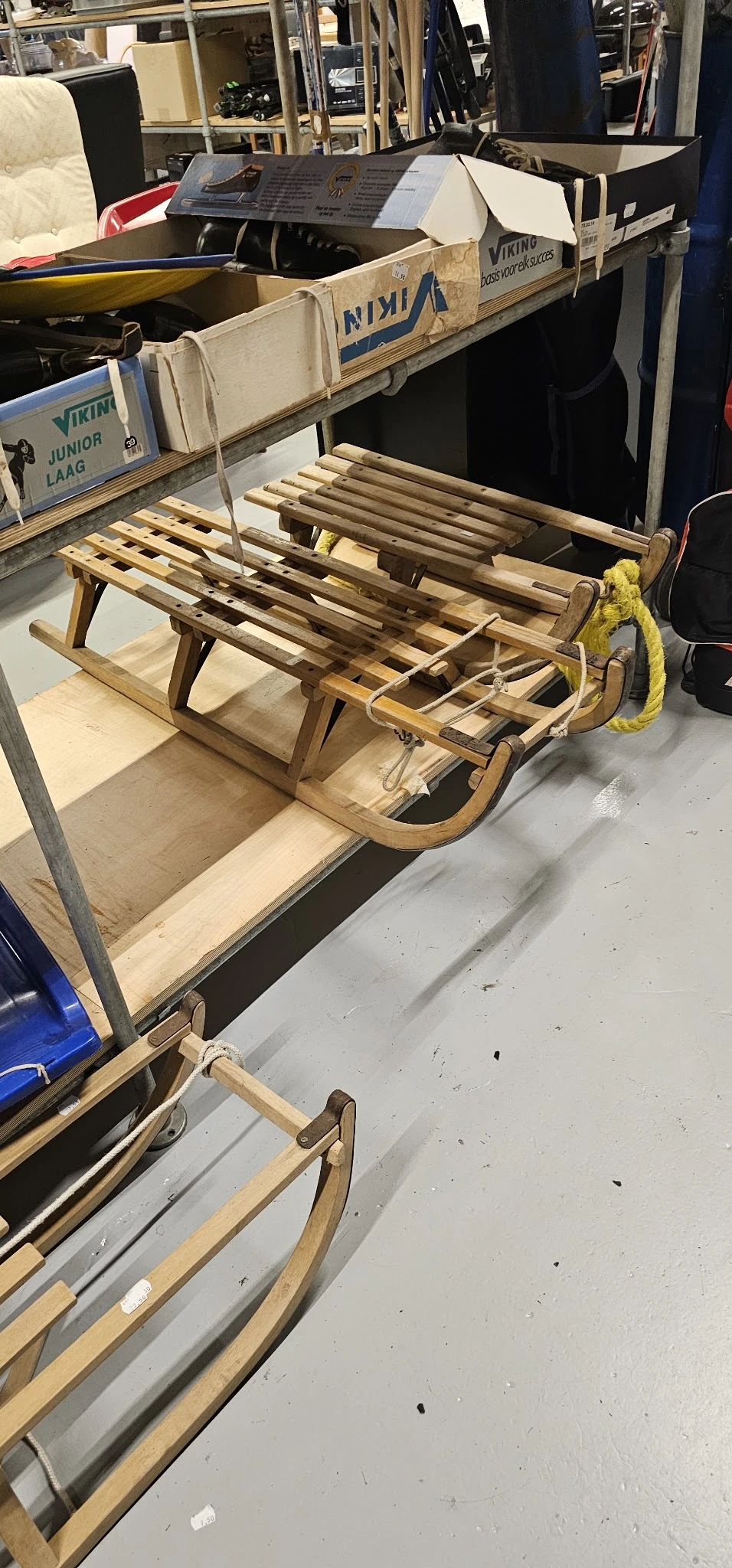 Houten slee met lattenbodem en geel touw, op opbergplank in kringloopwinkel