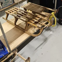 Houten slee met lattenbodem en geel touw, op opbergplank in kringloopwinkel