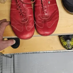 Close-up van twee rode leren schoenen met decoratieve stiksels, gemeten met een liniaal