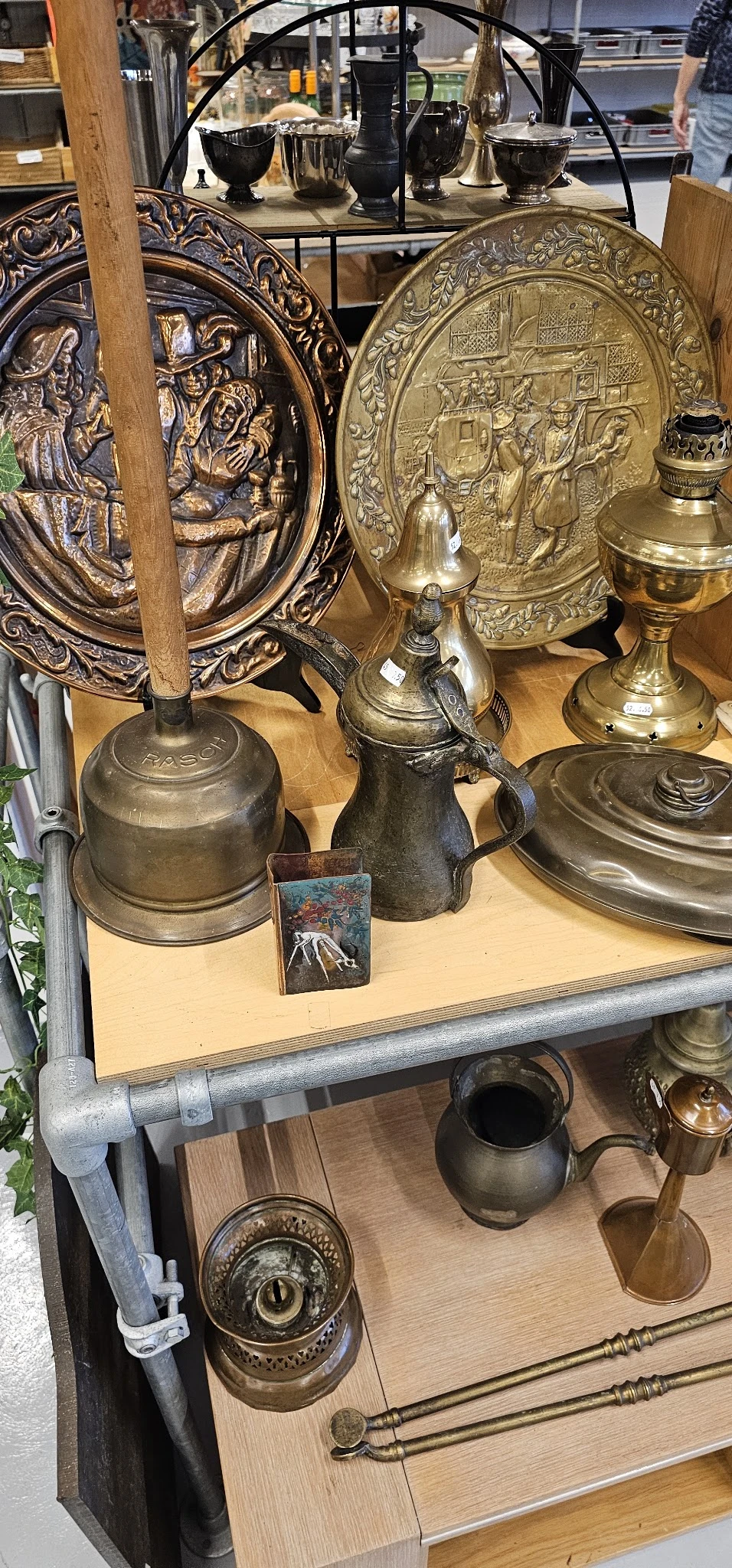 Uitgestalde antieke en vintage items: koperen en zilveren bellen, kannen, kelken en decoratieve objecten op houten plank