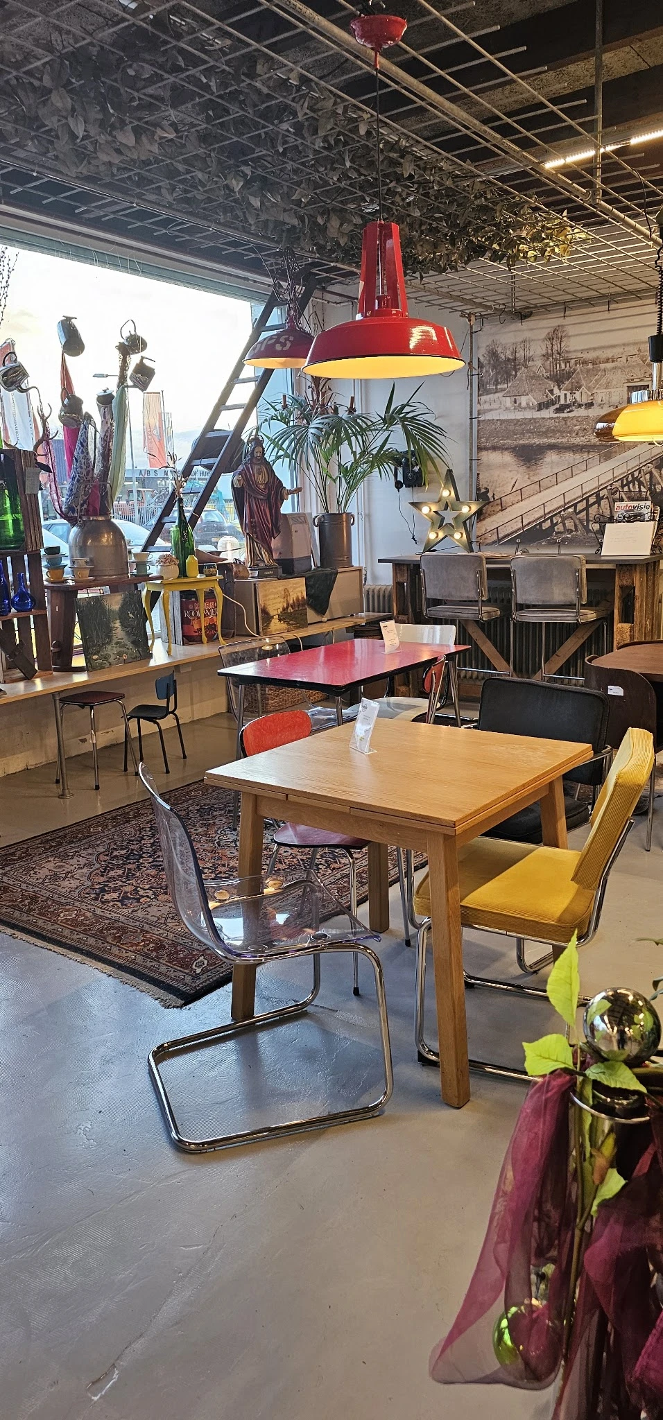 Winkelvloer met diverse meubels: houten eettafel met gekleurde stoelen, rode tafel op achtergrond, stellingen met decoratieve