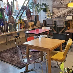Winkelvloer met diverse meubels: houten eettafel met gekleurde stoelen, rode tafel op achtergrond, stellingen met decoratieve