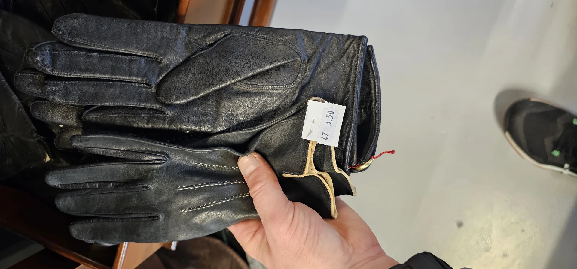 Zwarte leren handschoenen met geel accent, een daarvan wordt vastgehouden met een prijskaartje