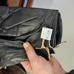 Zwarte leren handschoenen met geel accent, een daarvan wordt vastgehouden met een prijskaartje