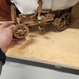 Close-up van een houten wiel van een miniatuurtrekwagen in iemands hand