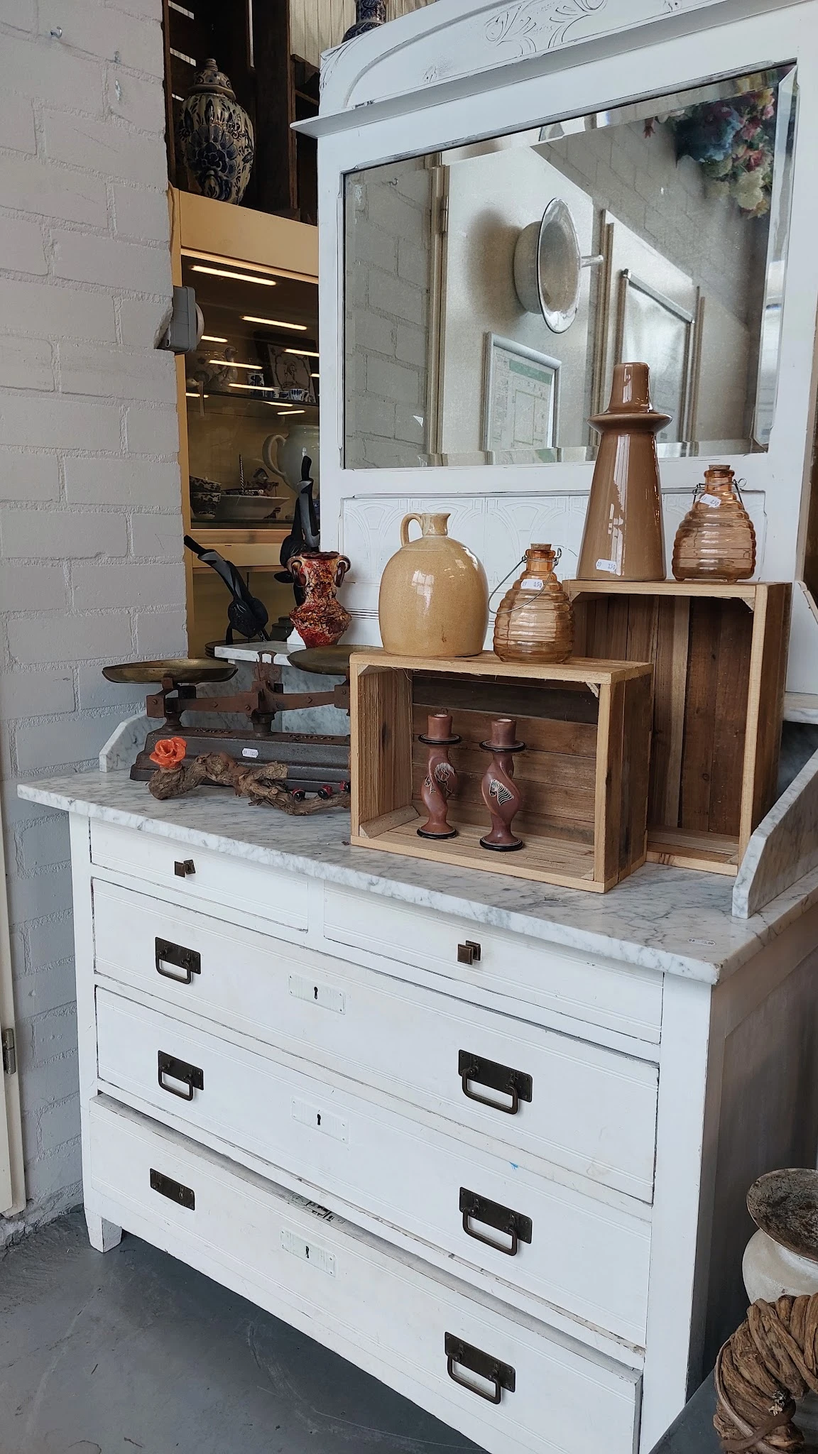 Uitgestalde decoratieve items: houten opbergkisten, keramische kruiken, koperen kandelaars en andere antieke voorwerpen op ee