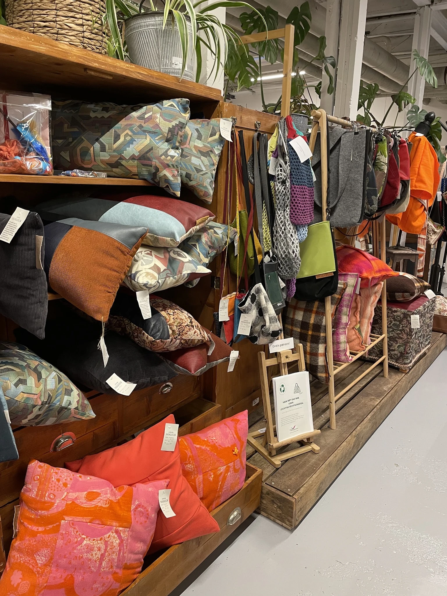 Uitgestalde tweedehands meubels en textielwaren in kringloopwinkel, waaronder bedden, kussens, dekens en kleding in verschill
