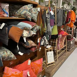 Uitgestalde tweedehands meubels en textielwaren in kringloopwinkel, waaronder bedden, kussens, dekens en kleding in verschill