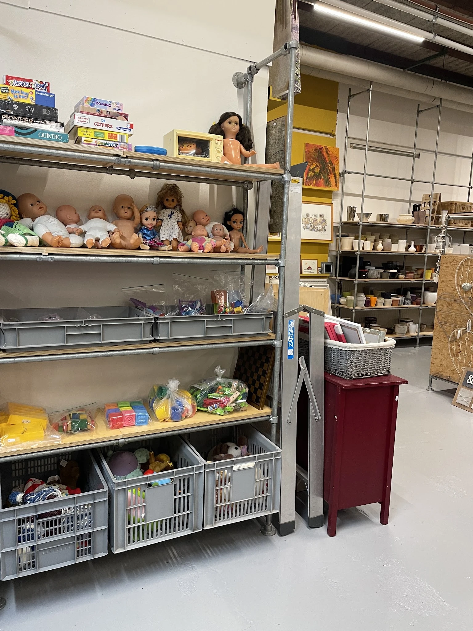 Glazen vitrinekast met poppenhuispoppen, speelgoed en diverse gebruiksartikelen in verschillende vakken