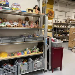 Glazen vitrinekast met poppenhuispoppen, speelgoed en diverse gebruiksartikelen in verschillende vakken