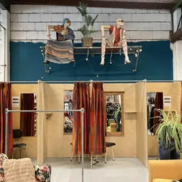 Winkelinterieur met kledingrekken, paskamers met rode gordijnen en displays aan de muur