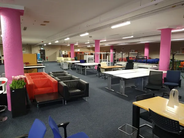 Ruim winkelinterieur met roze zuilen, werkplekken, zithoeken met oranje en zwarte stoelen, en blauwe vloer