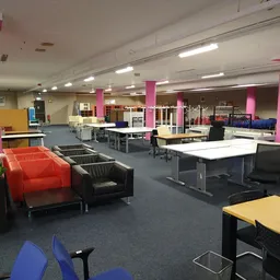 Ruim winkelinterieur met roze zuilen, werkplekken, zithoeken met oranje en zwarte stoelen, en blauwe vloer