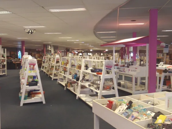 Ruim winkelbinnenland met witte display-kasten en paarse zuilen, volgesteld met diverse tweedehands artikelen