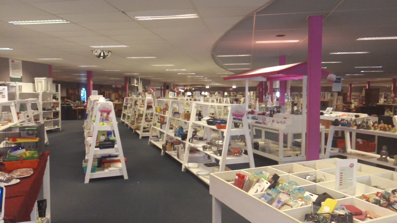 Ruim winkelbinnenland met witte display-kasten en paarse zuilen, volgesteld met diverse tweedehands artikelen