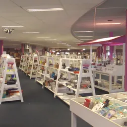 Ruim winkelbinnenland met witte display-kasten en paarse zuilen, volgesteld met diverse tweedehands artikelen