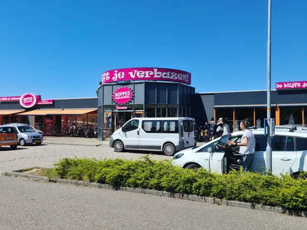 Voorkant kringloopwinkel met fuchsia gevel en logo, parkeerplaats met auto's