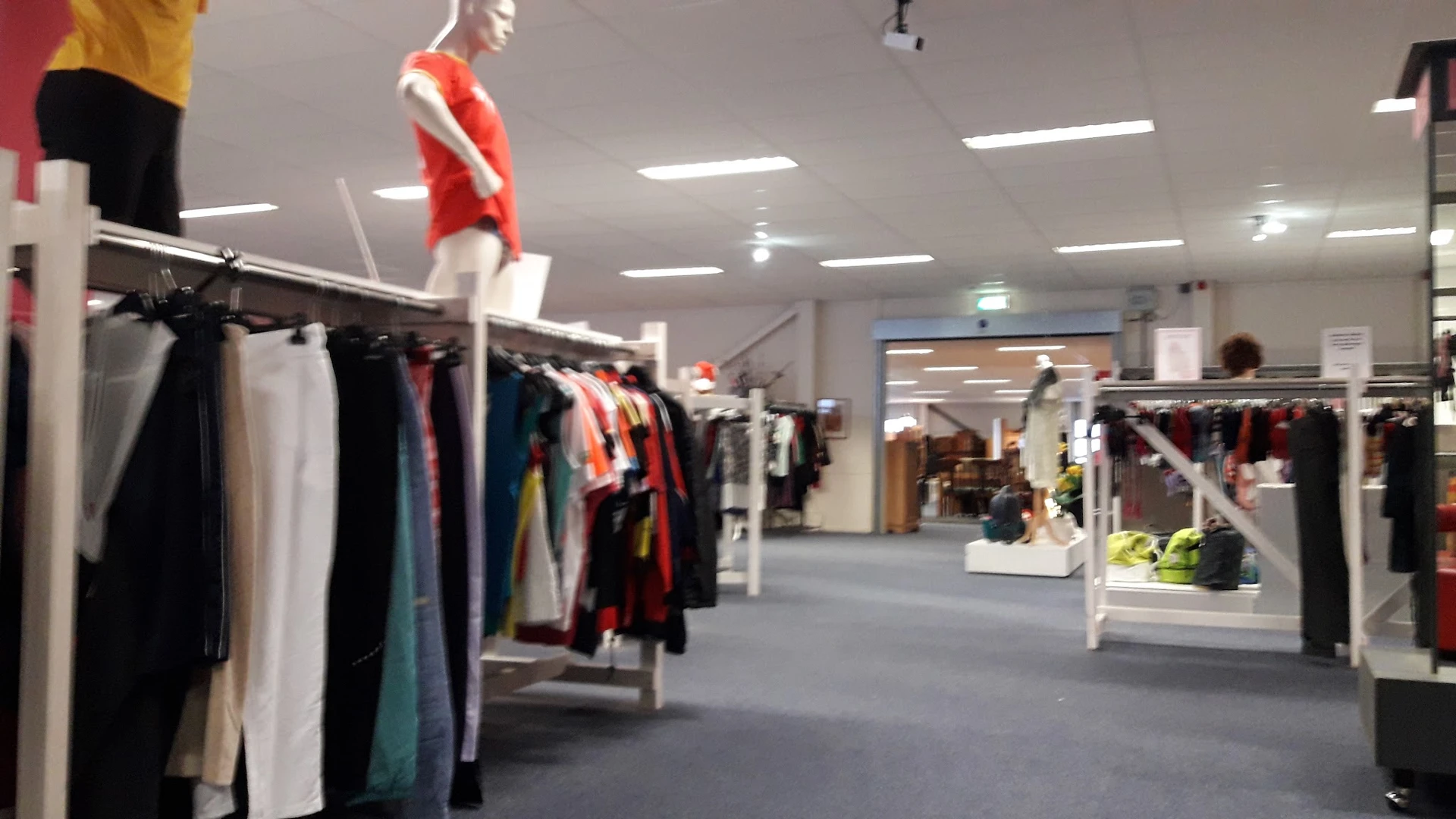 Winkelvloer met kledingrekken en mannequin in rode jurk, moderne winkelruimte met plafondverlichting