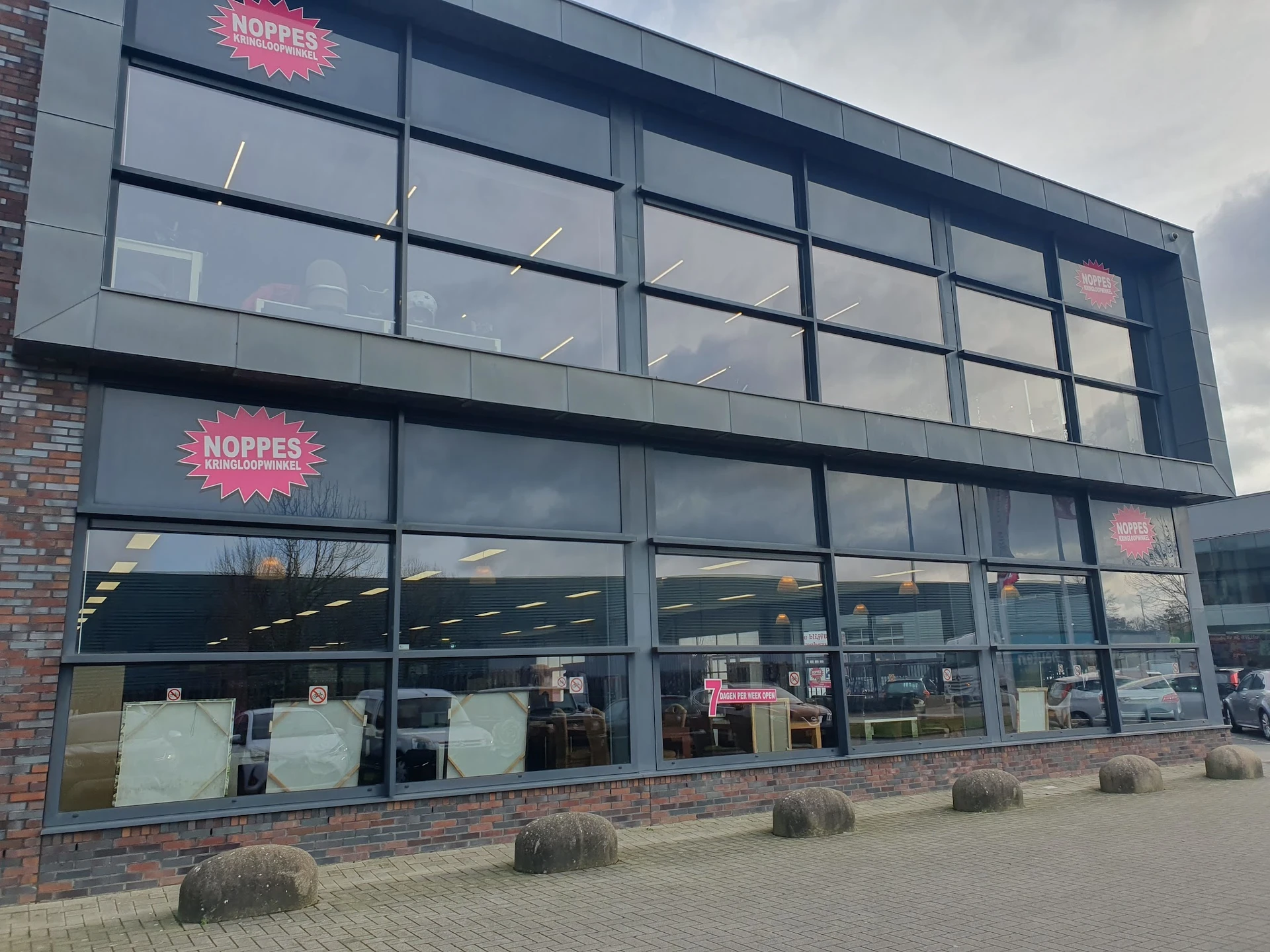 Gevel van kringloopwinkel Noppes met grote glazen pui, twee verdiepingen en roze logobordes