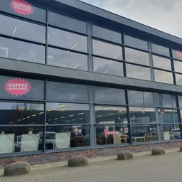 Gevel van kringloopwinkel Noppes met grote glazen pui, twee verdiepingen en roze logobordes