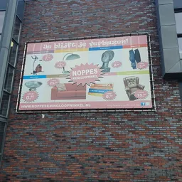 Reclamebord van kringloopwinkel Noppes tegen bakstenen muur met foto's van meubels en huishoudelijke artikelen