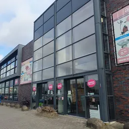 Voorgevel van kringloopwinkel met grote ramen, donkerblauwe pui en roze borden met 'NOPPES' letters