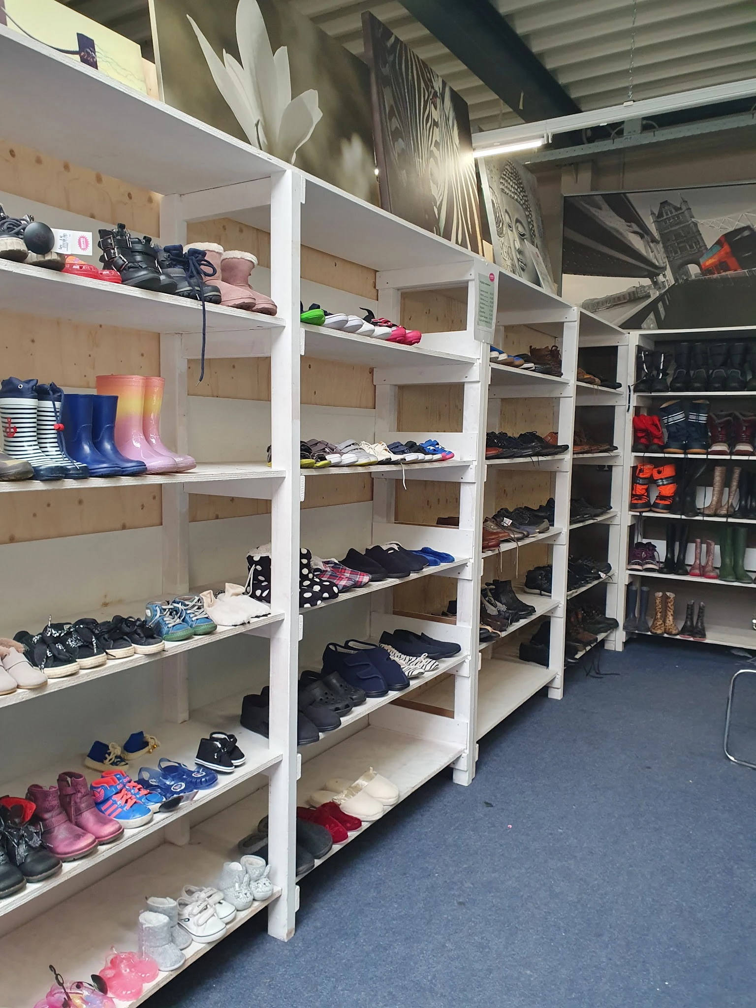 Witte stellingen met tweedehands kleding, schoenen en accessoires netjes uitgestald
