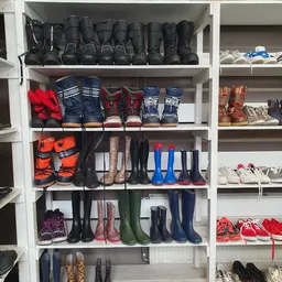 Witte stellingen met uitgestalde kinderschoenen, laarzen en sportschoenen in verschillende kleuren