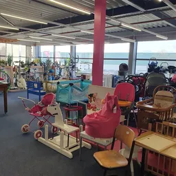 Speelgoed en kinderspullen in een kringloopwinkel met grote ramen en uitzicht op water
