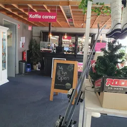 Koffiehoek in kringloopwinkel met toonbank, bord 'nu open', koelkasten en winkelrekken op achtergrond