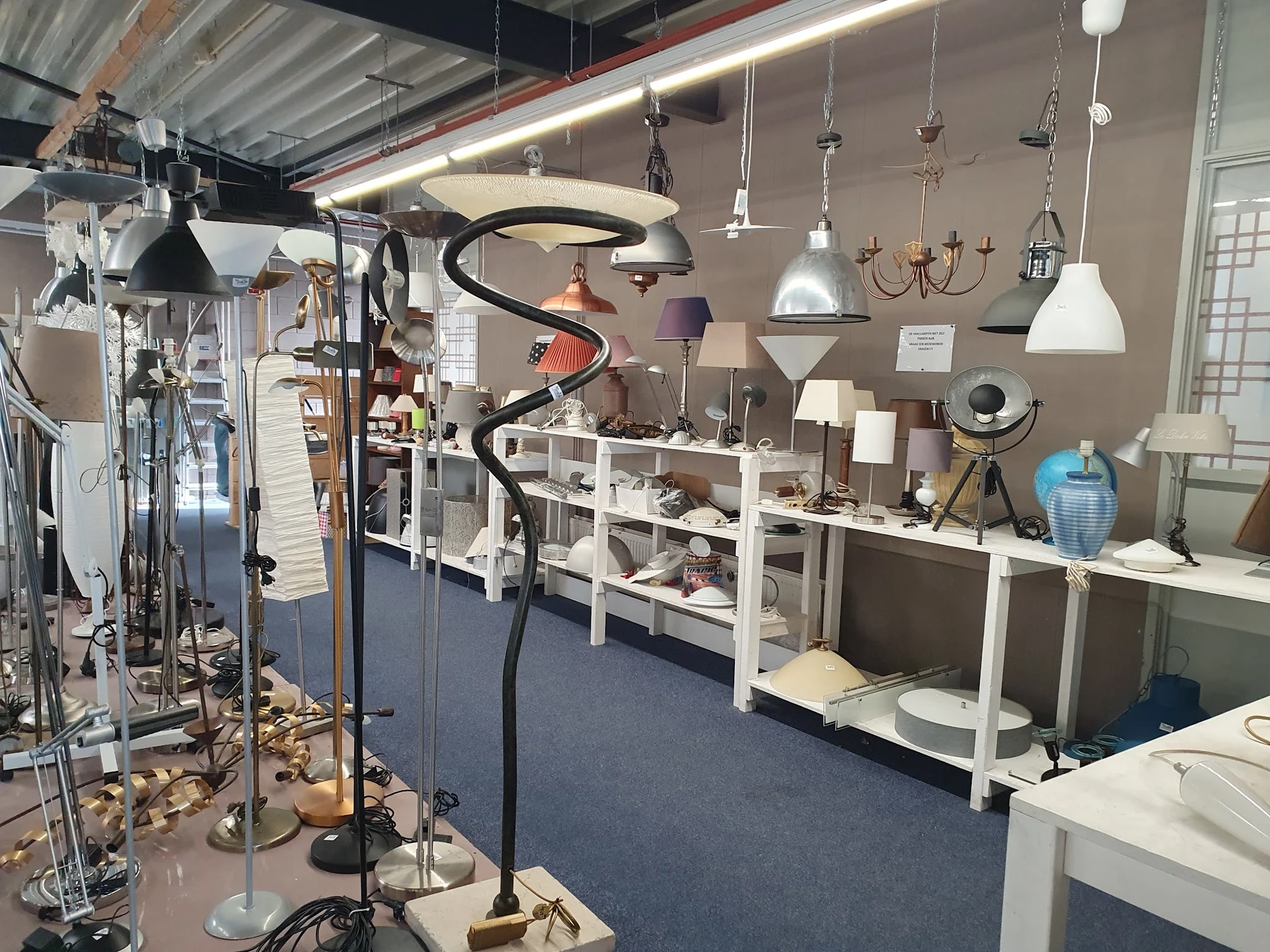 Winkelinterieur met witte stellingen vol huishoudelijke artikelen, hangende lampen en decorstukken