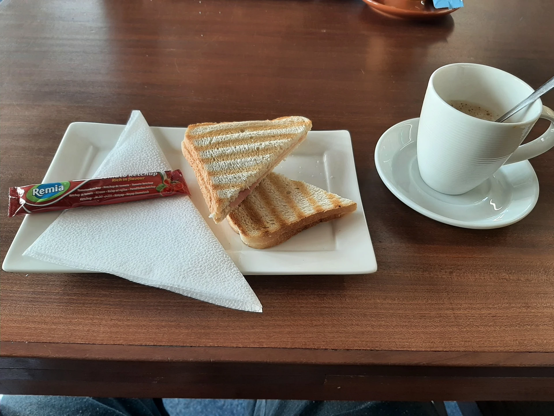 Twee geroosterde boterhammen, servette, boterham met beleg en koffiekopje op schotel op houten tafel