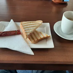 Twee geroosterde boterhammen, servette, boterham met beleg en koffiekopje op schotel op houten tafel