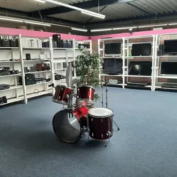 Interieur van kringloopwinkel met witte stellingen vol elektronische apparatuur, drums en een plant op de vloer