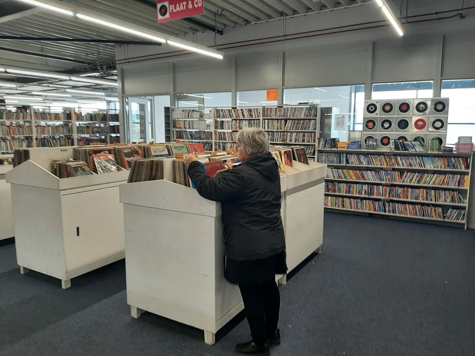 Winkelvloer met witte bakkenkast en CD-rekken, klant bladert door media-aanbod