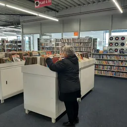 Winkelvloer met witte bakkenkast en CD-rekken, klant bladert door media-aanbod