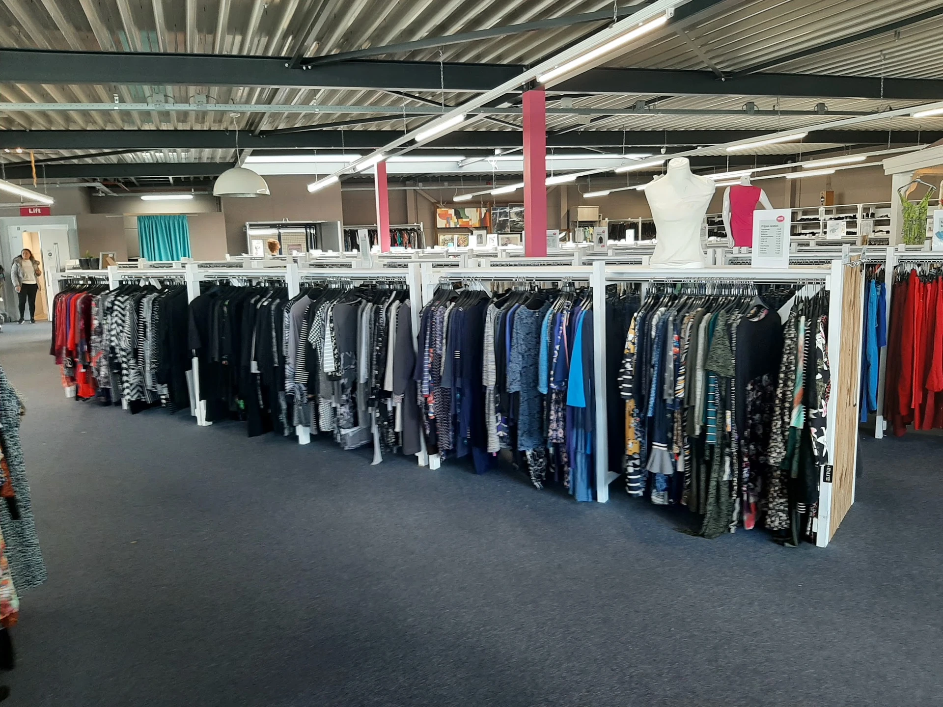 Rekken met tweedehands kleding in verschillende kleuren, met name jassen en truien netjes uitgestald in de winkel