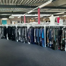 Rekken met tweedehands kleding in verschillende kleuren, met name jassen en truien netjes uitgestald in de winkel