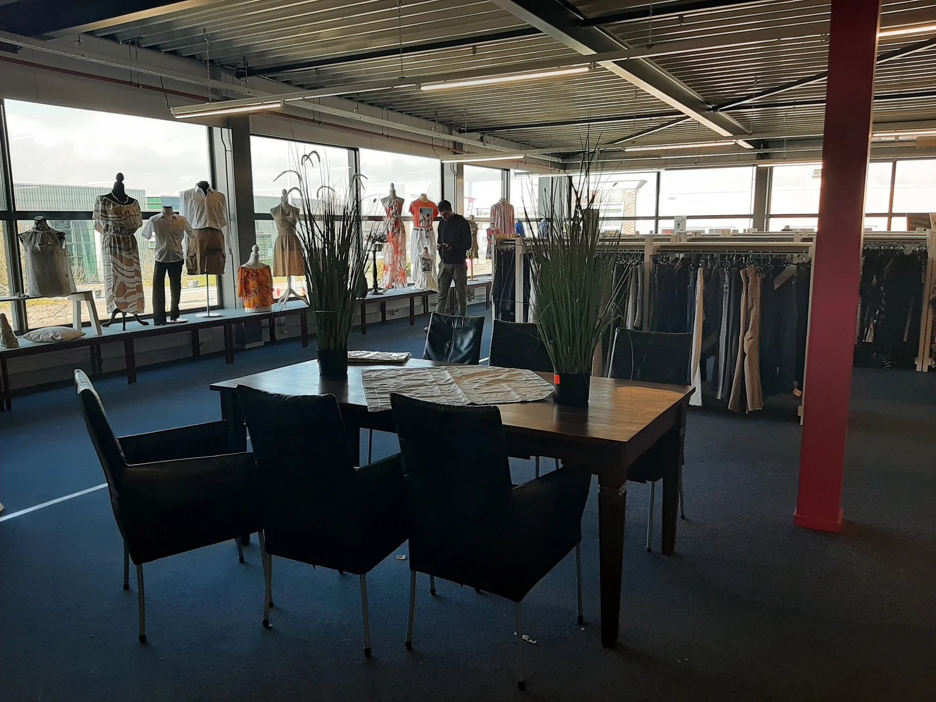 Ruime winkelruimte met kledingrekken, etalagepoppen en een tafel met stoelen in het voorplan