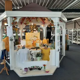 Uitgestalde kledingcollectie in een wit display met herfstdecoratie, bloemen en gele kledingstukken op mannequins