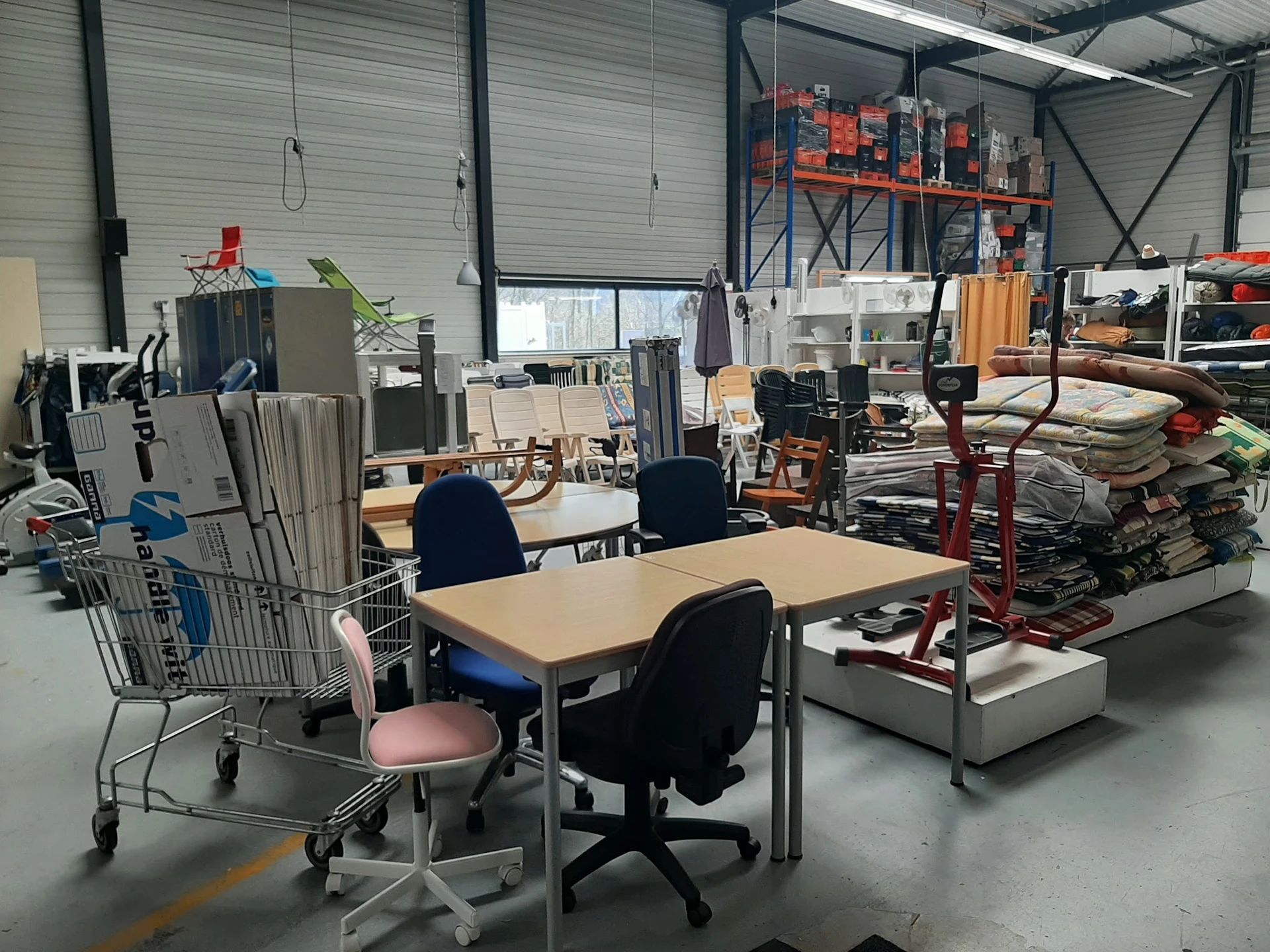 Werkruimte in kringloopwinkel met tafel, bureaustoelen, stellingen met spullen en diverse items
