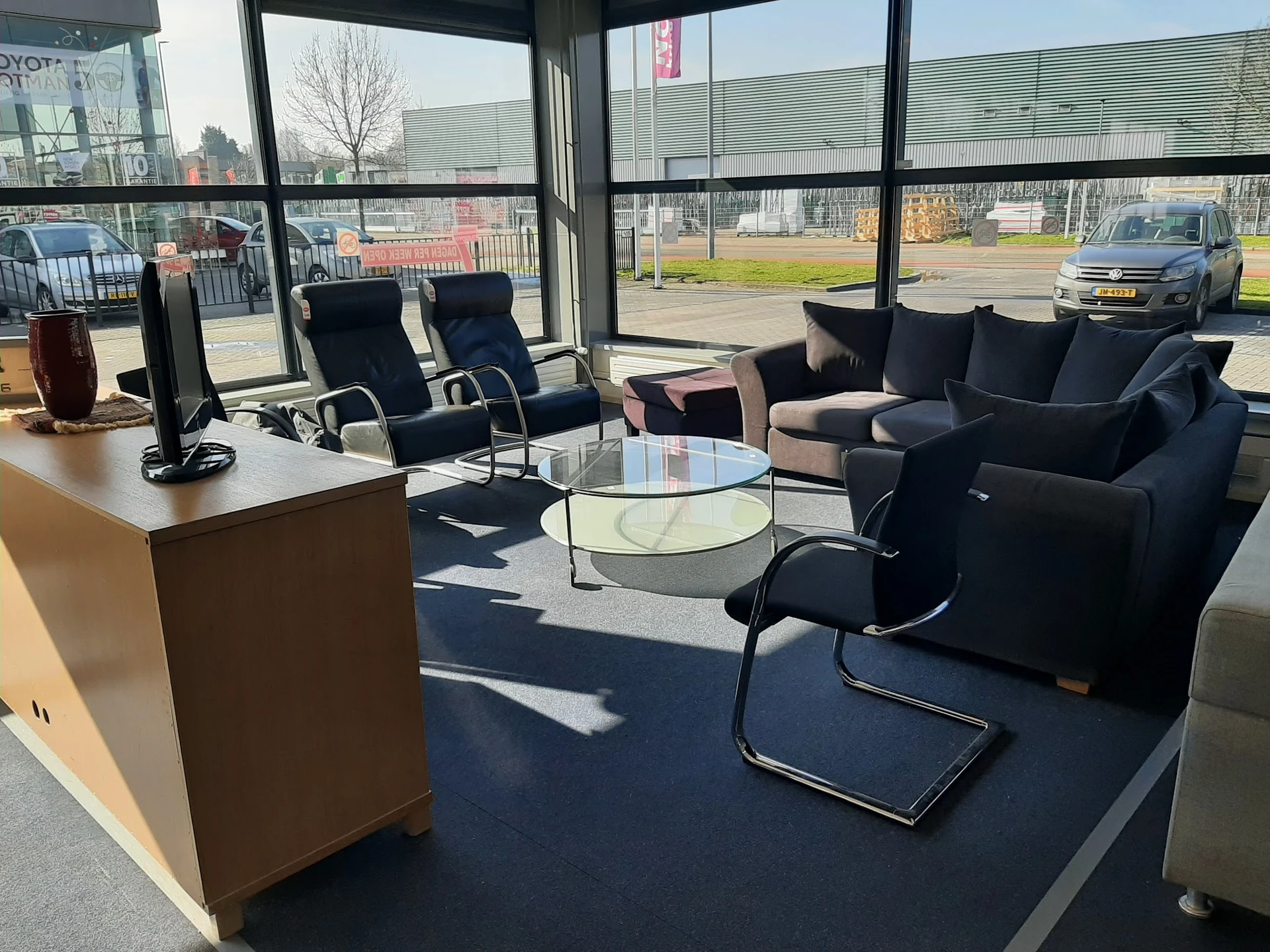 Sfeervolle zithoek met zwarte fauteuils, glazen tafel en bruine kast in kringloopwinkel