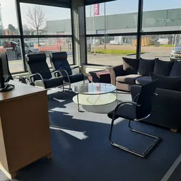 Sfeervolle zithoek met zwarte fauteuils, glazen tafel en bruine kast in kringloopwinkel