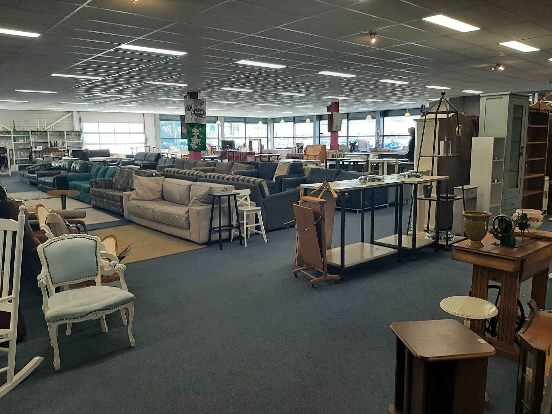 Winkelvloer met diverse meubels: banken, stoelen, tafels en kasten uitgestald in een ruime kringloopwinkel
