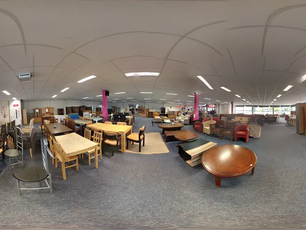 Ruim winkelvloer met houten meubels, tafels, stoelen en diverse inrichtingsstukken in een kringloopwinkel